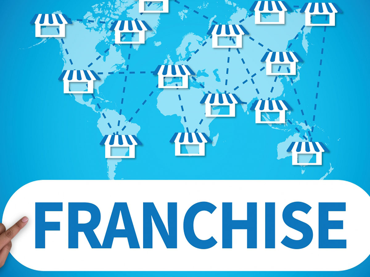 Businessman points to a whiteboard that says “franchise” and shows a map of franchise locations. 